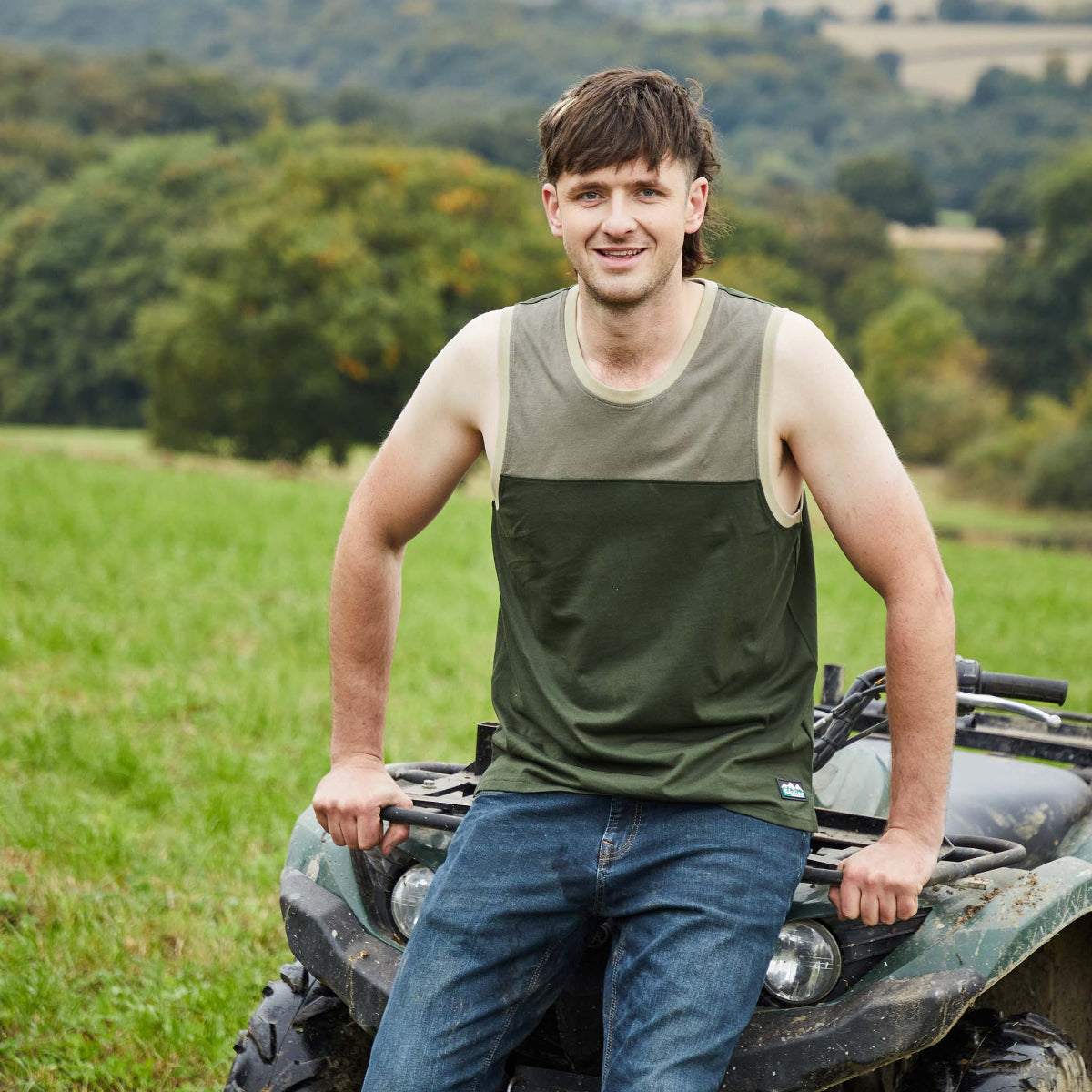 Man sitting on a quad bike in a field with trees in the background