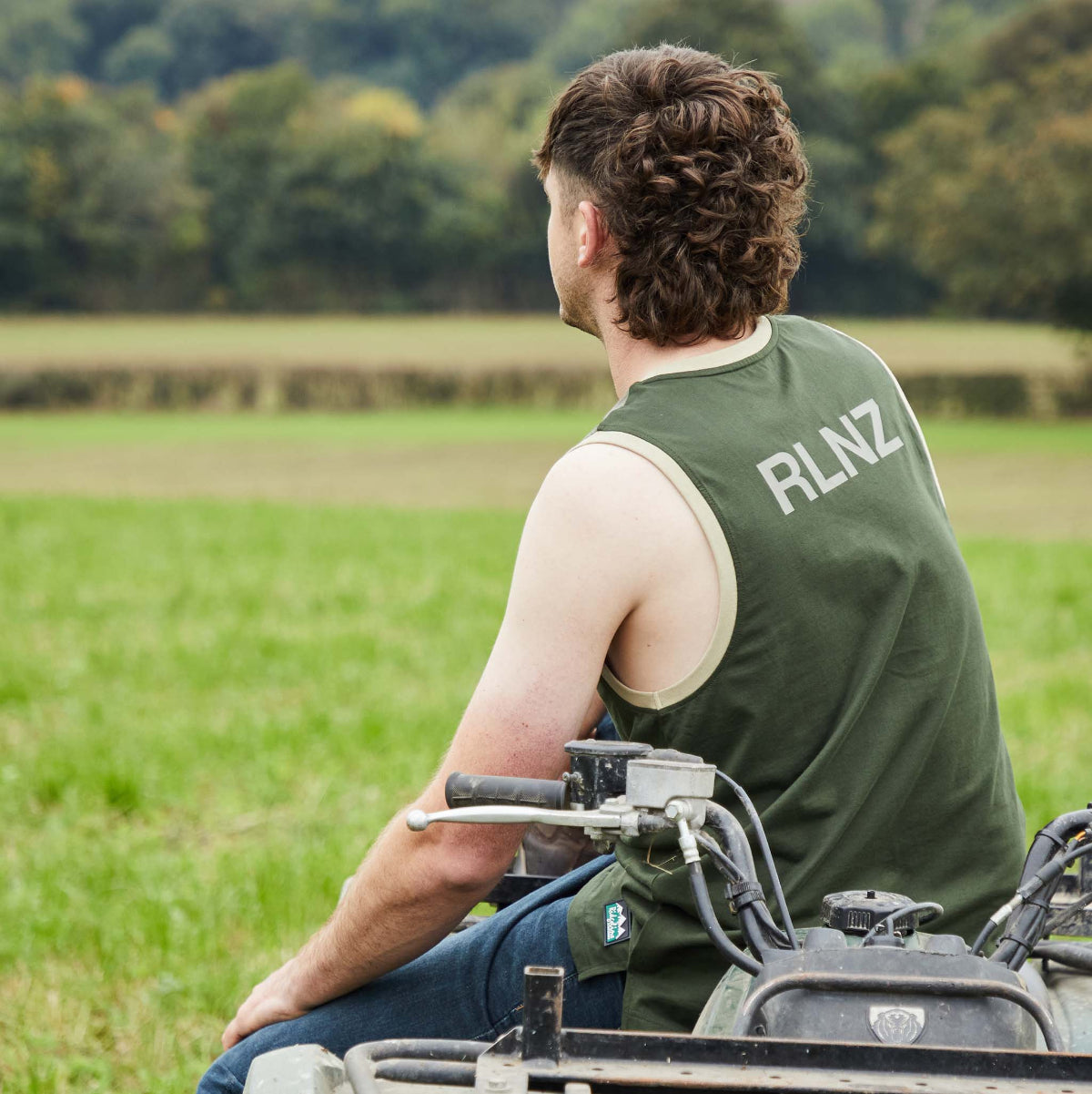 Man sitting on a four-wheeler in a field with 'RLNZ' on his shirt