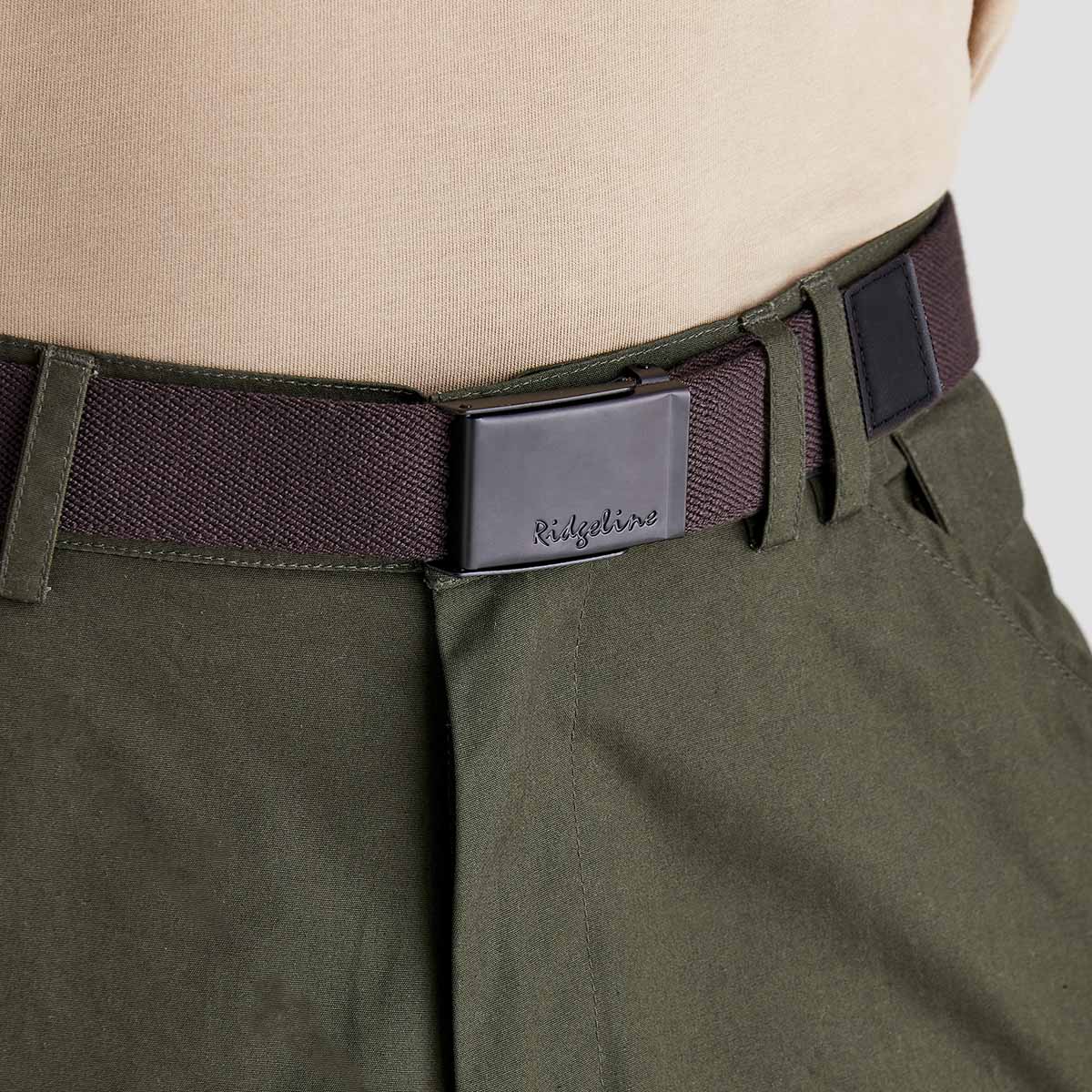 Ridgeline brown woven fabric belt with embossed logo on black plaque buckle, worn with trousers, angled close-up. Ridgeline inscribed on it.
