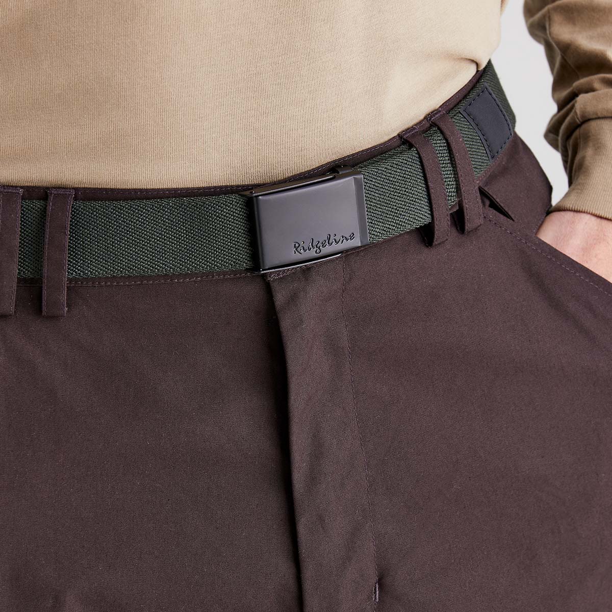 Ridgeline green woven fabric belt with Ridgeline‑inscribed black plaque buckle, worn with trousers, angled close-up