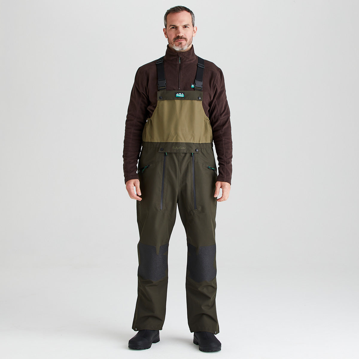 Man wearing a brown flecce and green overalls on a white background