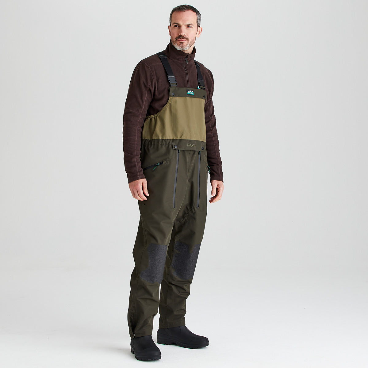 Man wearing a brown jacket and green waders/ bib & brace on a white background
