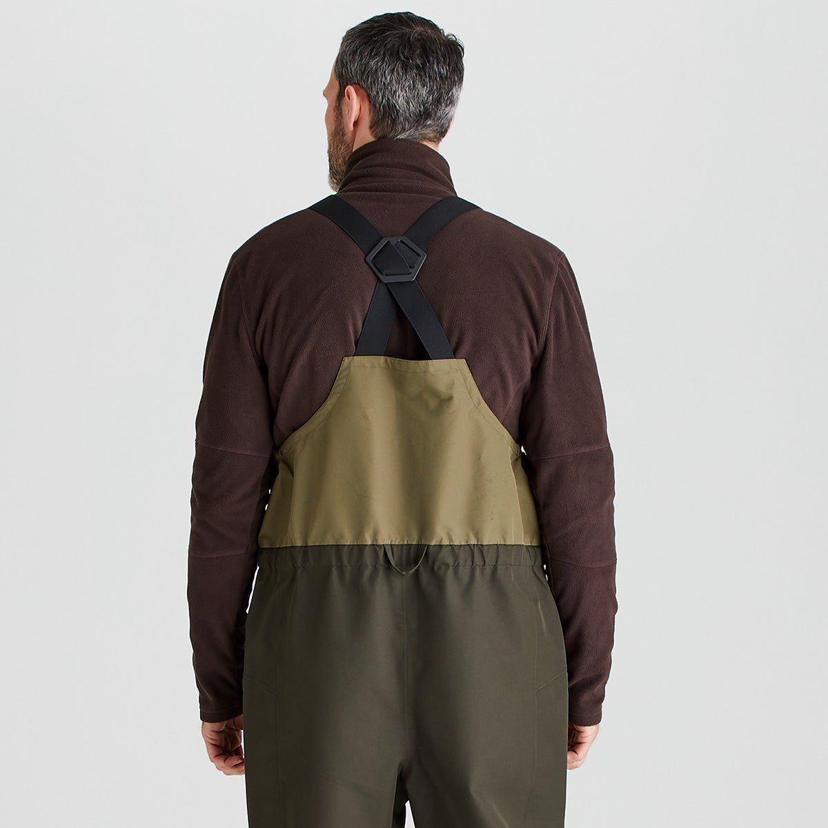 Man wearing a brown fleece and green overalls on a light gray background