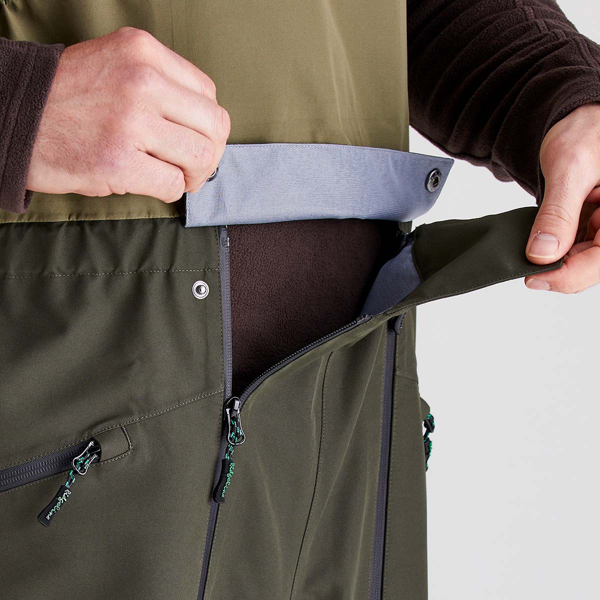 Person adjusting a green bib & brace with a gray lining on a light gray background