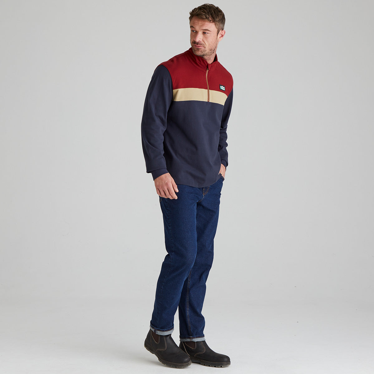 Man wearing a colorful pullover and jeans on a gray background