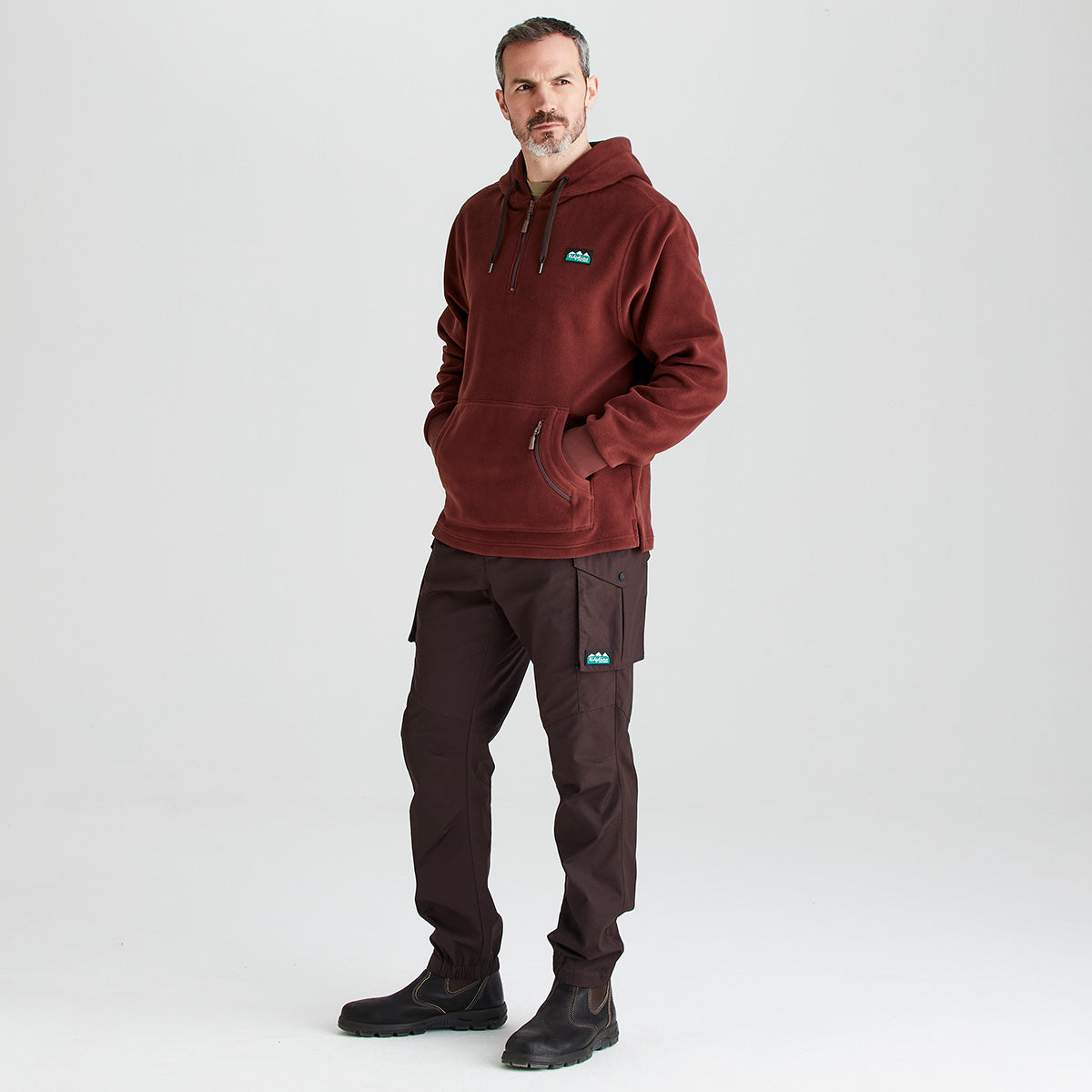 Man wearing a brown hoodie and pants with a logo on a white background