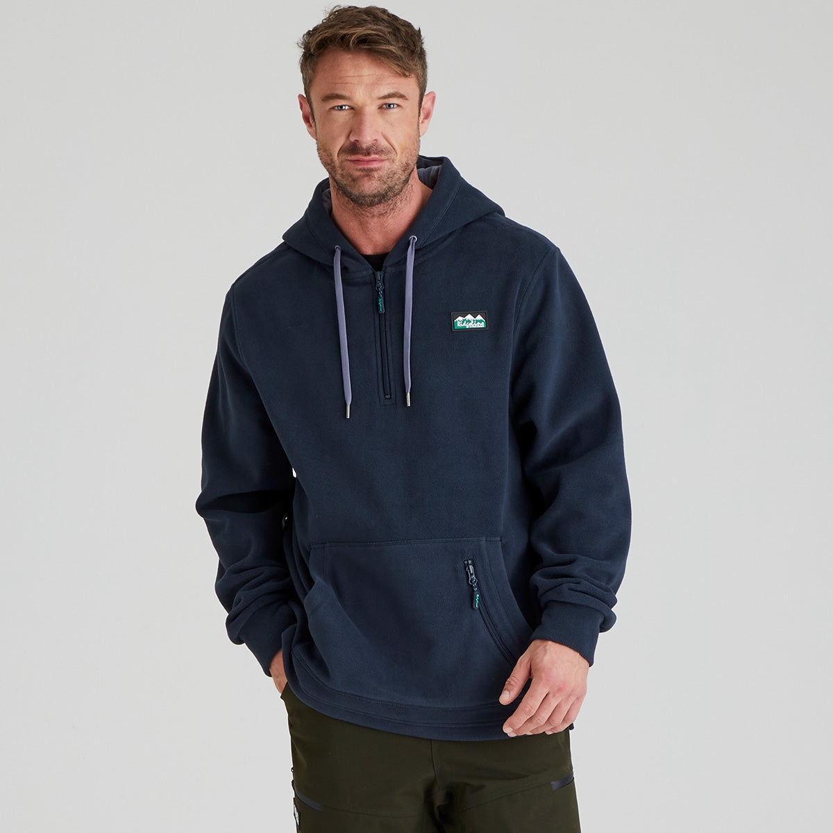 Man wearing a navy blue fleece hoodie with a ridgeline clothing logo on a grey background