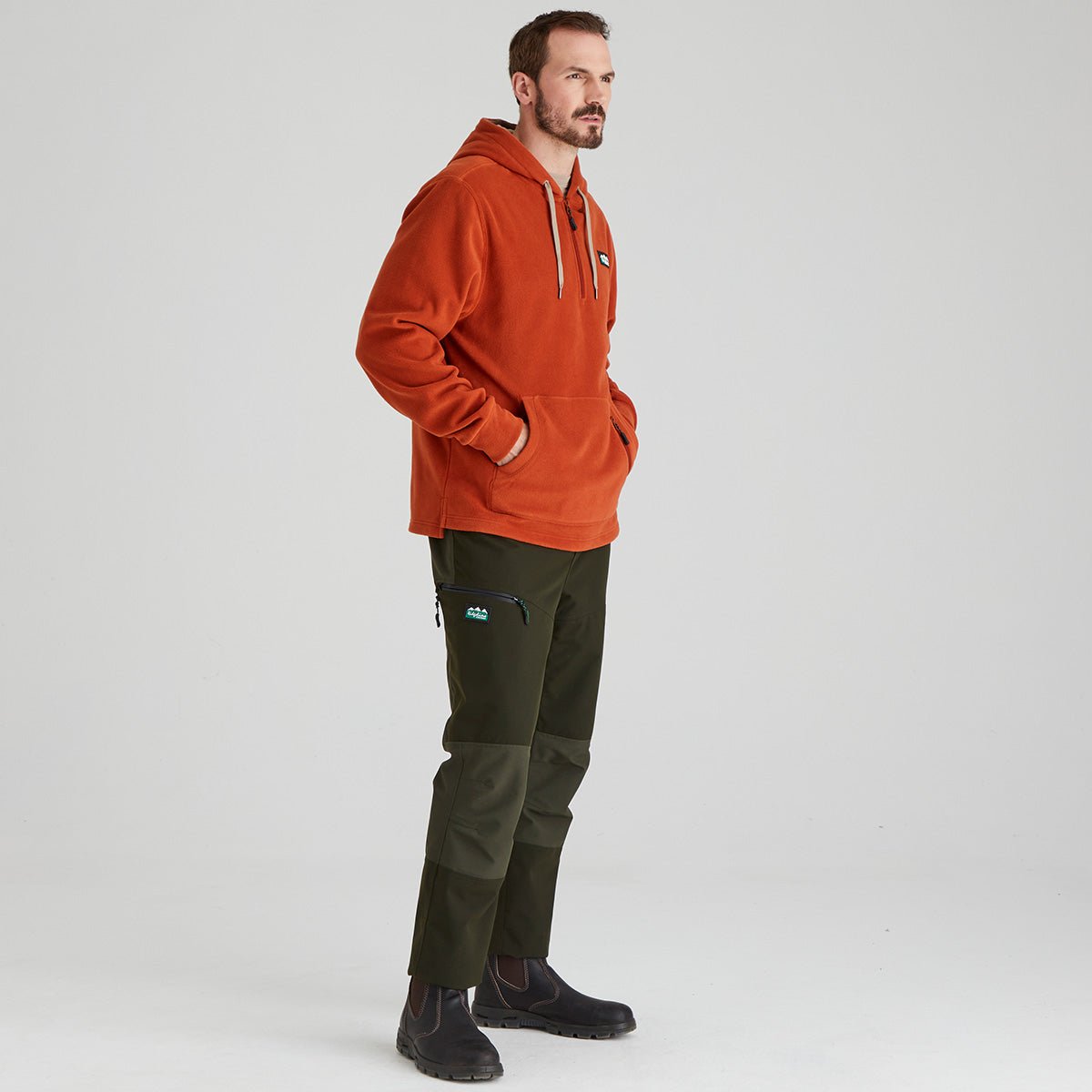 Man wearing an orange hoodie and green pants on a white background