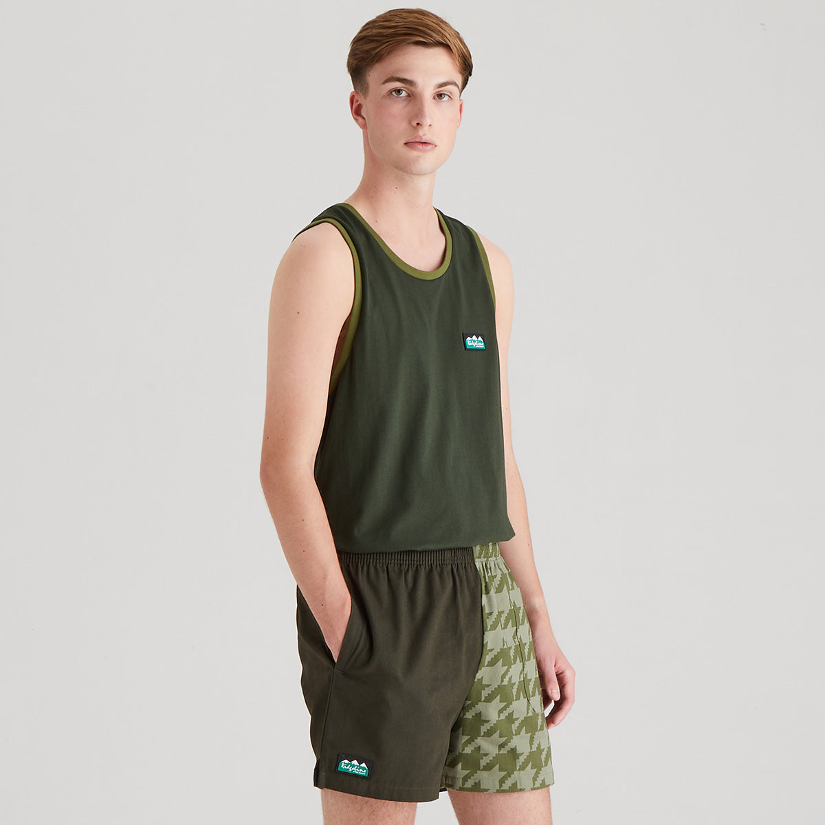 Person wearing a green tank top and shorts with a logo on a light gray background