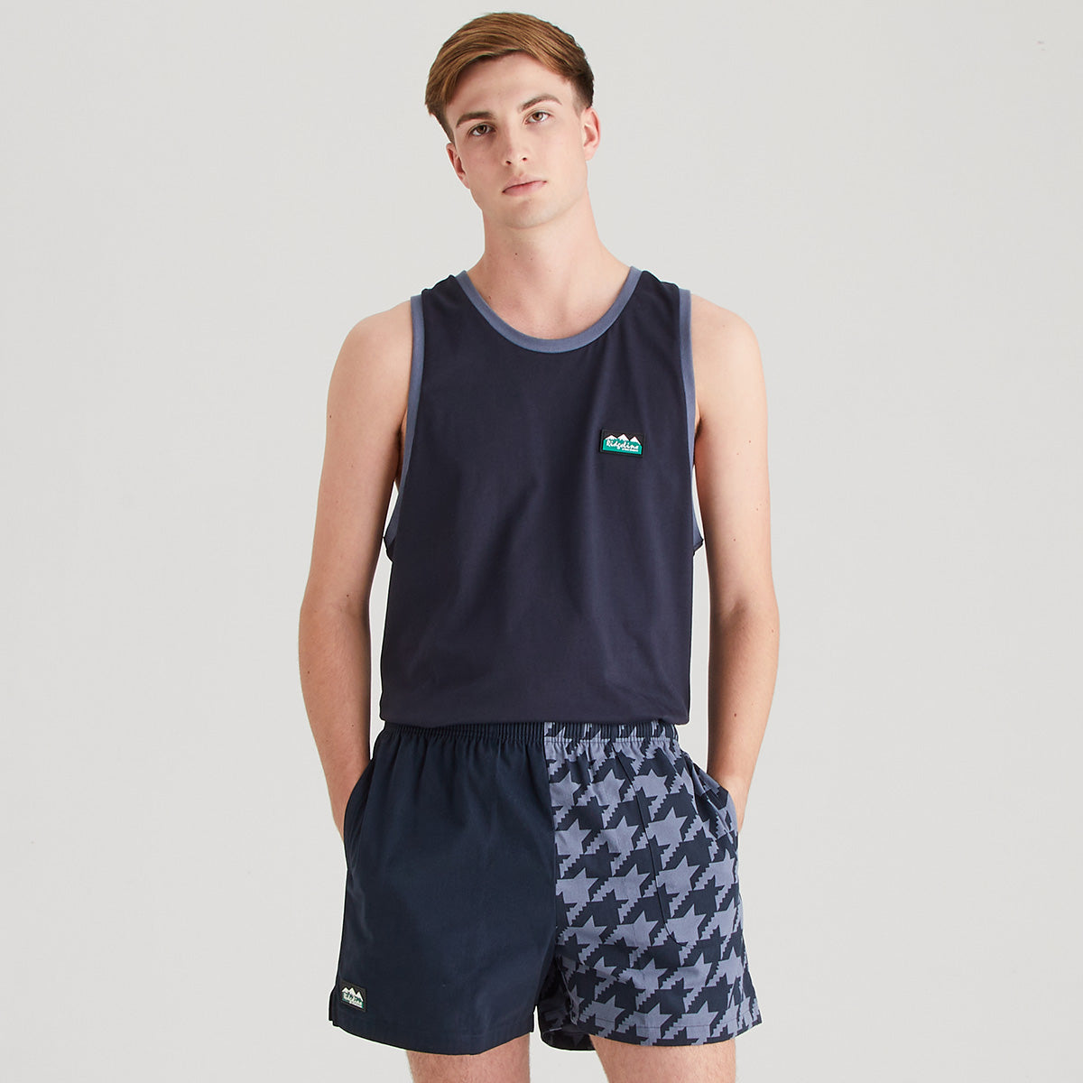 Man wearing a navy tank top and patterned shorts on a light gray background