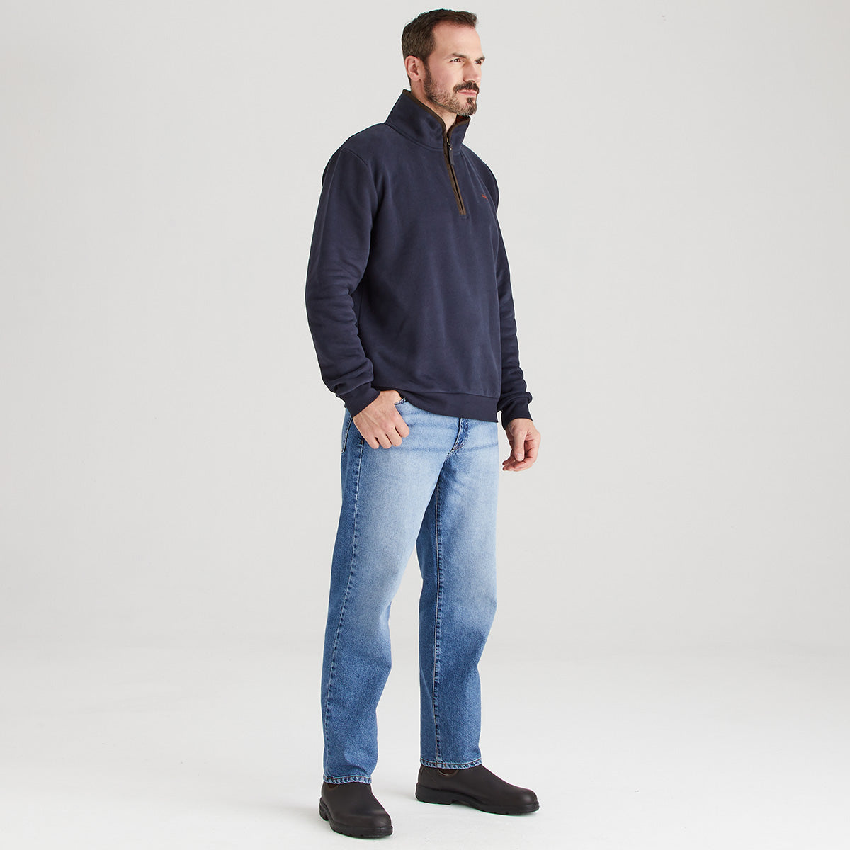 Man wearing a navy fleece pullover and light blue jeans on a white background