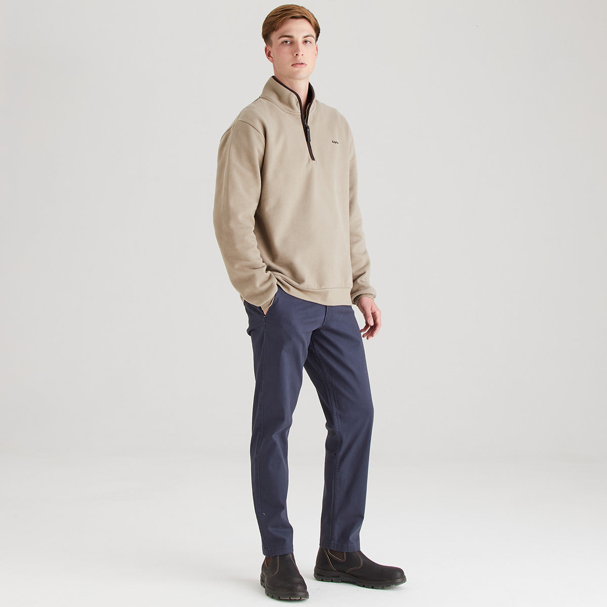 Man wearing a beige pullover and navy pants on a white background