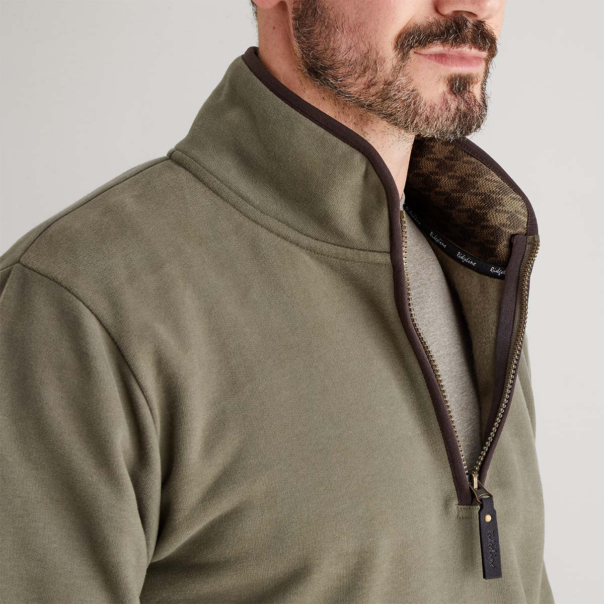 Close-up of a person wearing a green zip jumper with a brand logo on a light gray background
