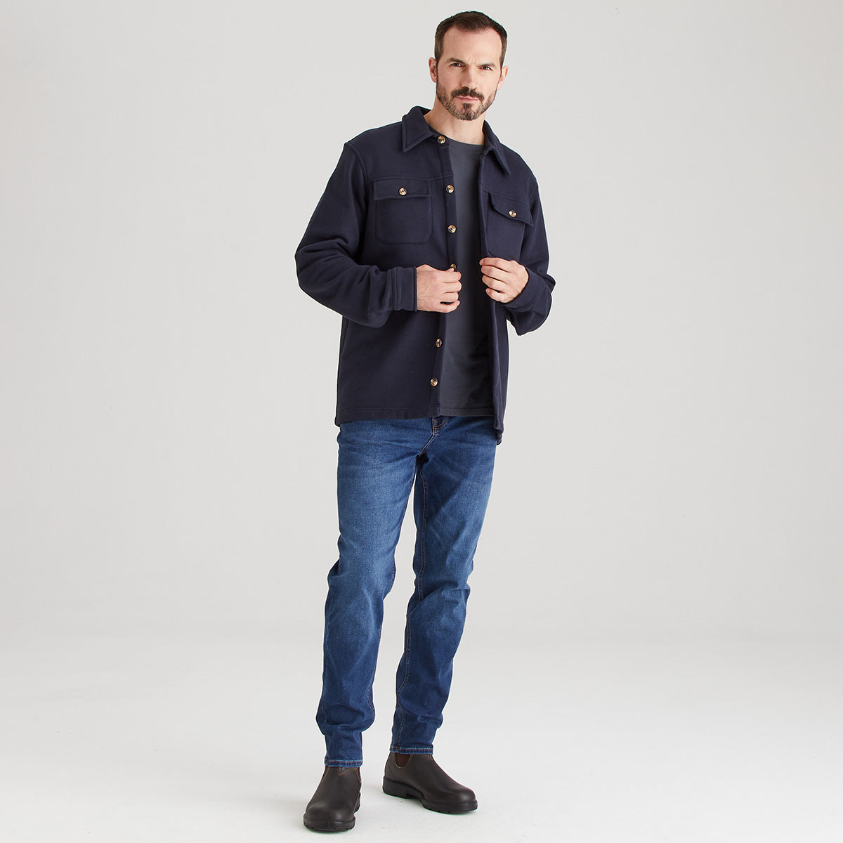 Man wearing a navy jacket and blue jeans on a white background