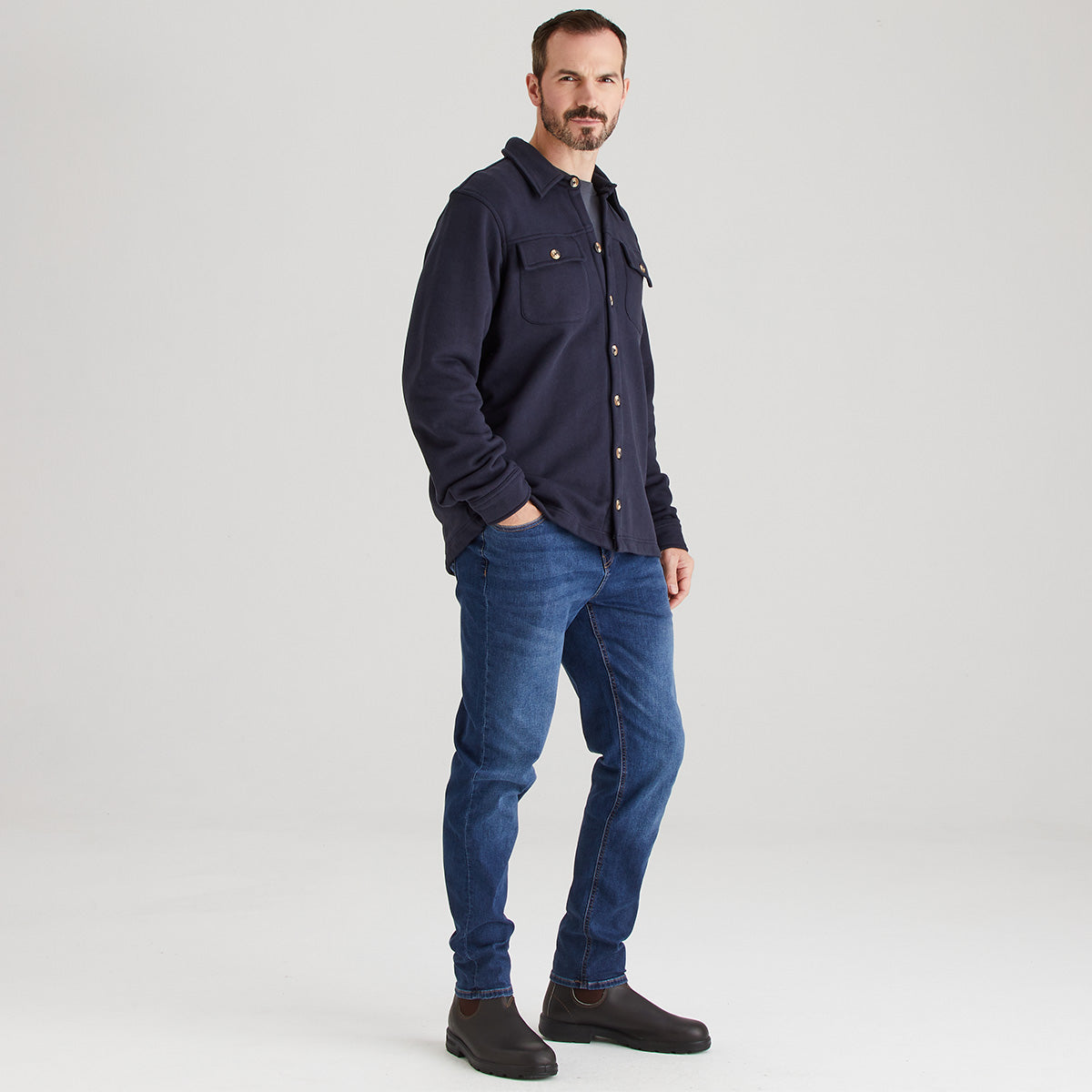 Man wearing a navy shirt and blue jeans on a white background