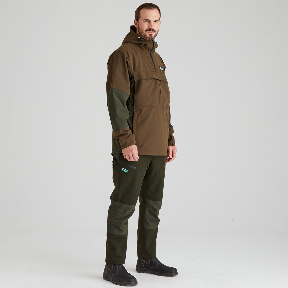 Man wearing a brown and green jacket and pants on a light grey background