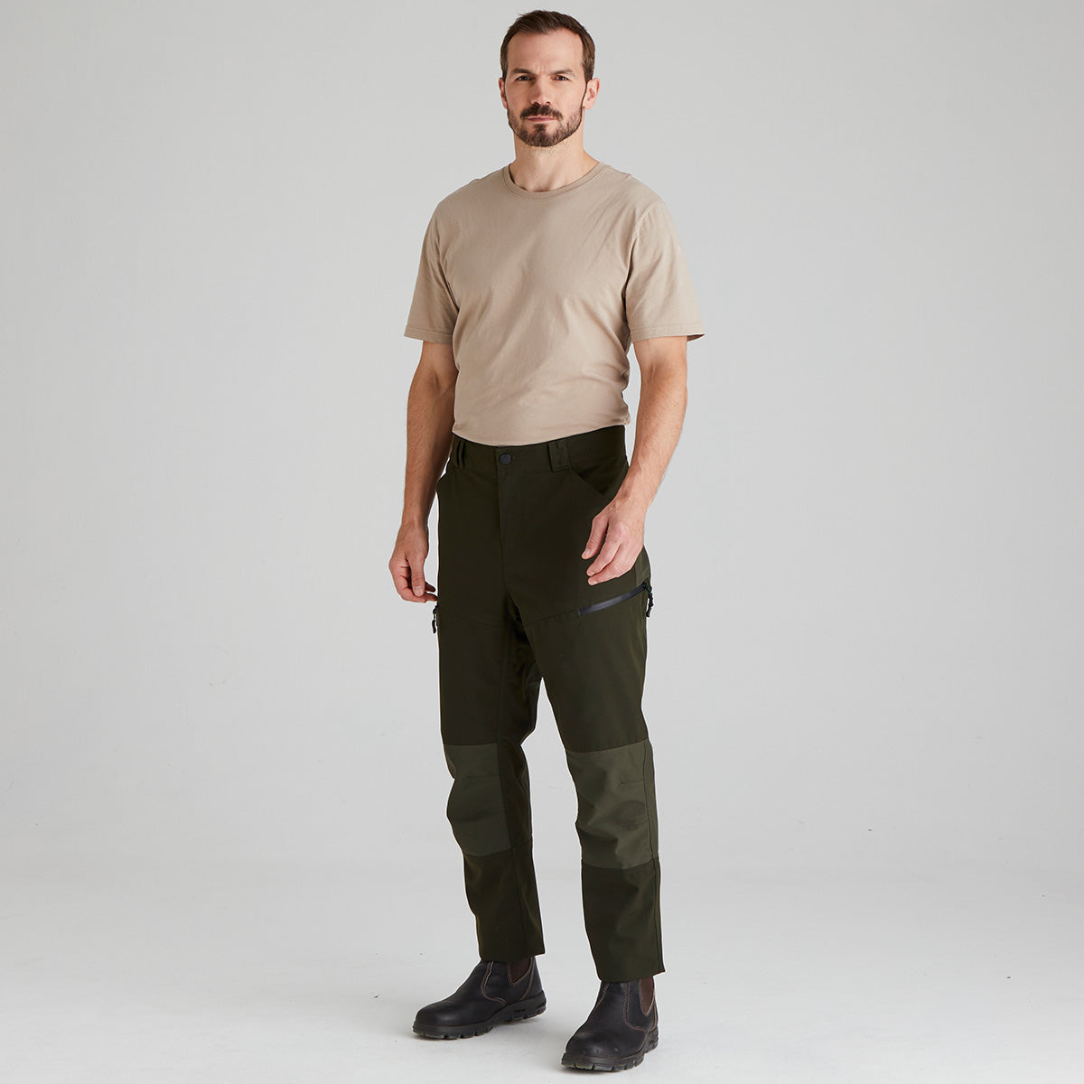 Man wearing a beige t-shirt and green pants on a white background