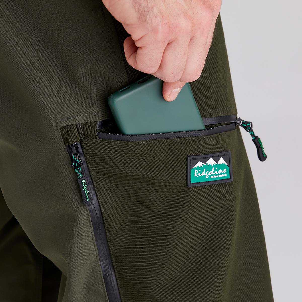 Person placing a green phone case into a pocket of a green jacket with a visible brand logo.