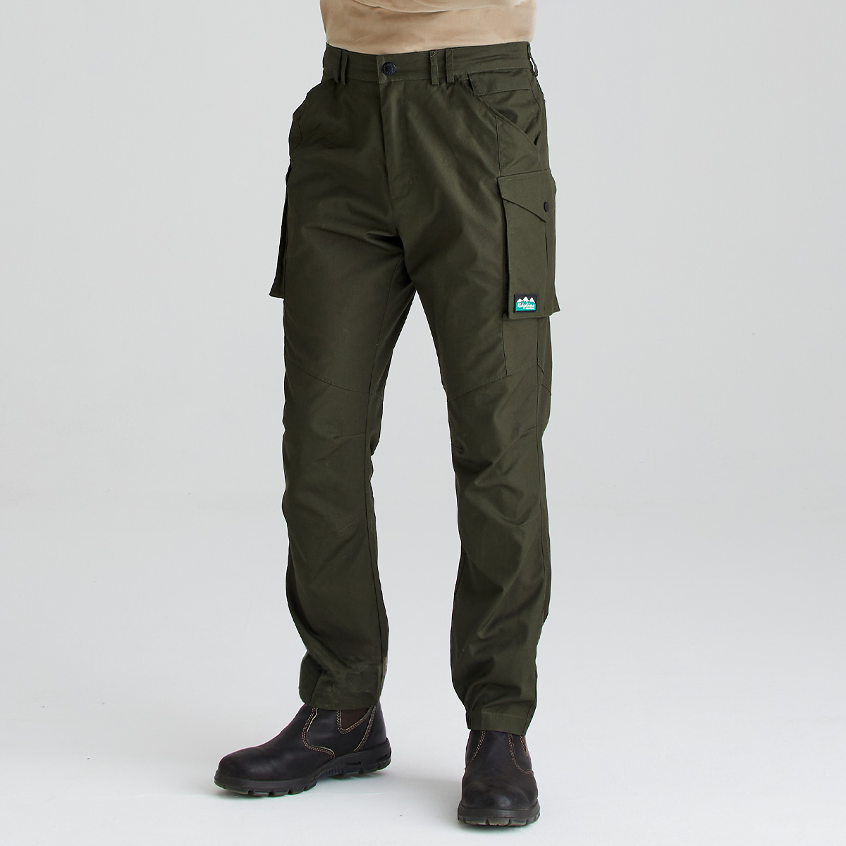 A person wearing dark olive green cargo pants with side flap pockets and elastic ankle cuffs, paired with dark brown boots, shown against a light gray studio background.