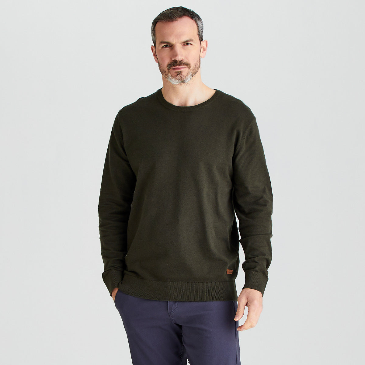 Man wearing a dark green sweater and purple pants on a light gray background