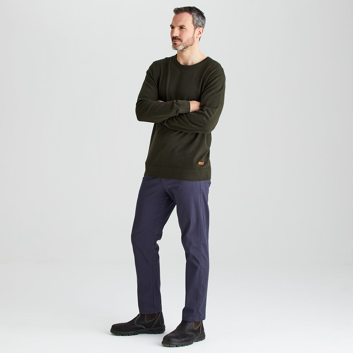 Man wearing a green sweater and dark pants on a white background