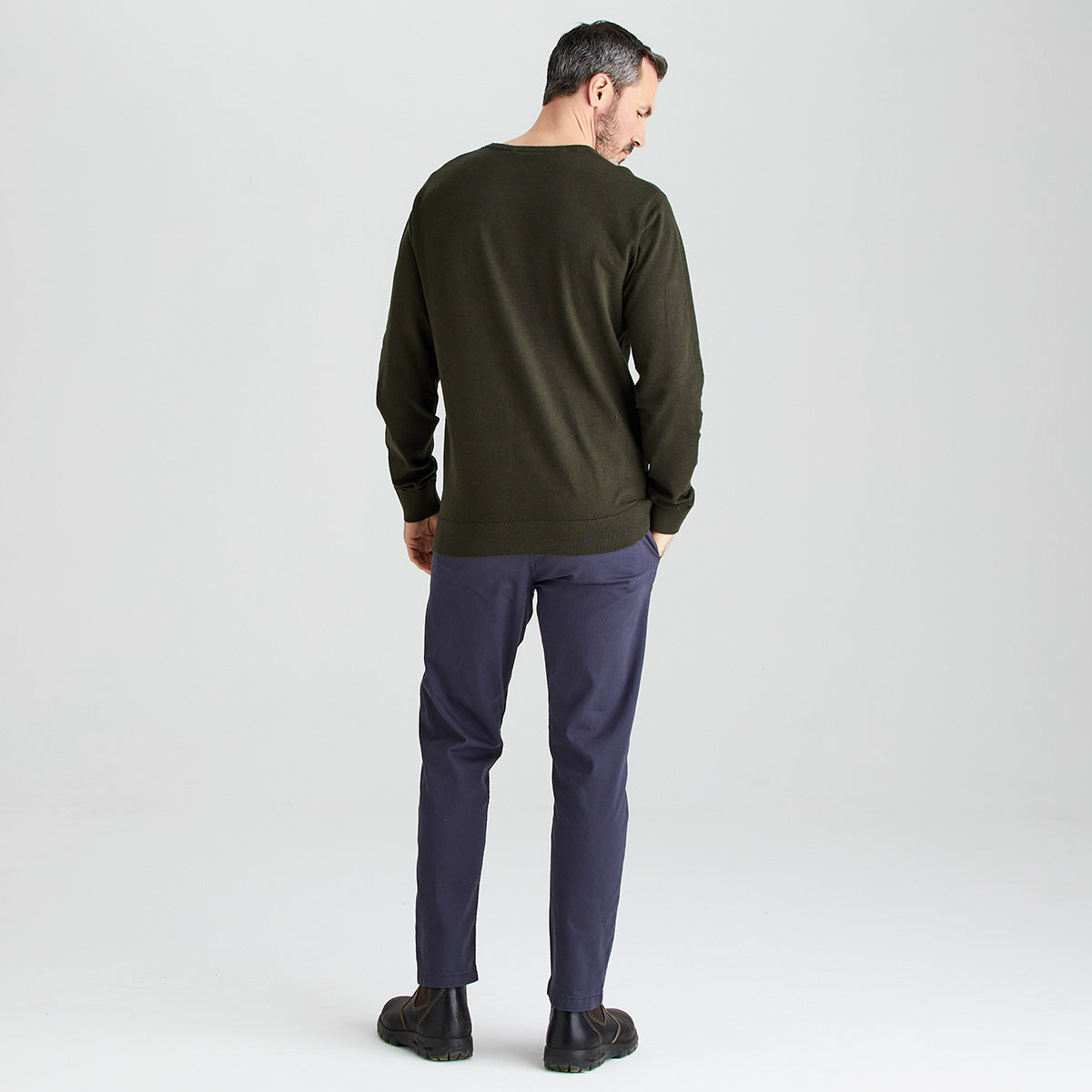 Man wearing an olive green sweater and navy pants on a white background