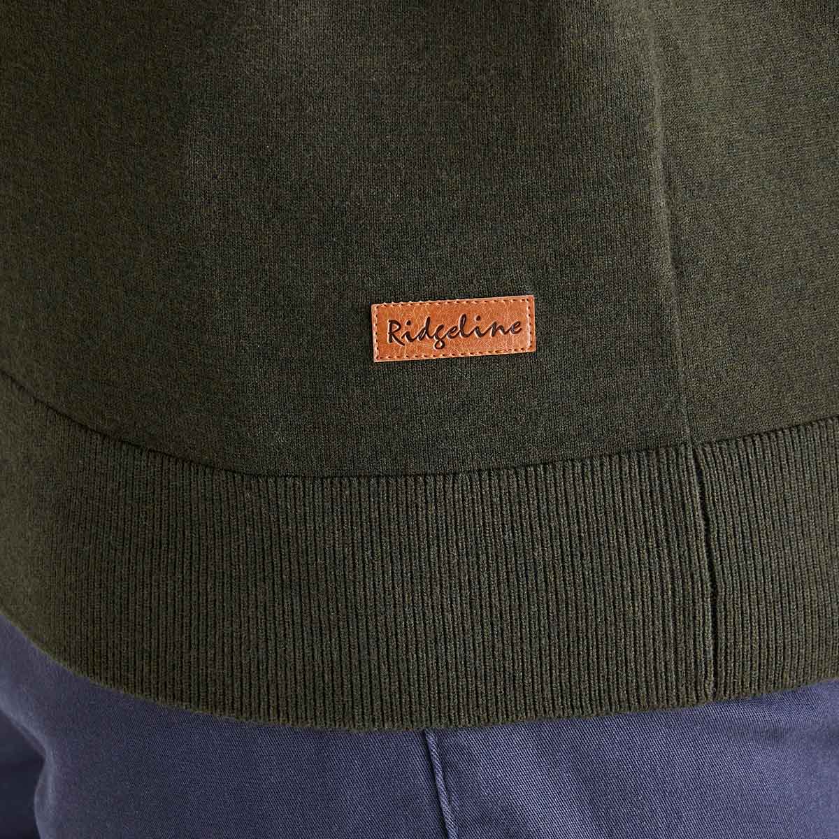 Close-up of a green jacket with a brand label on the chest, worn over blue pants.