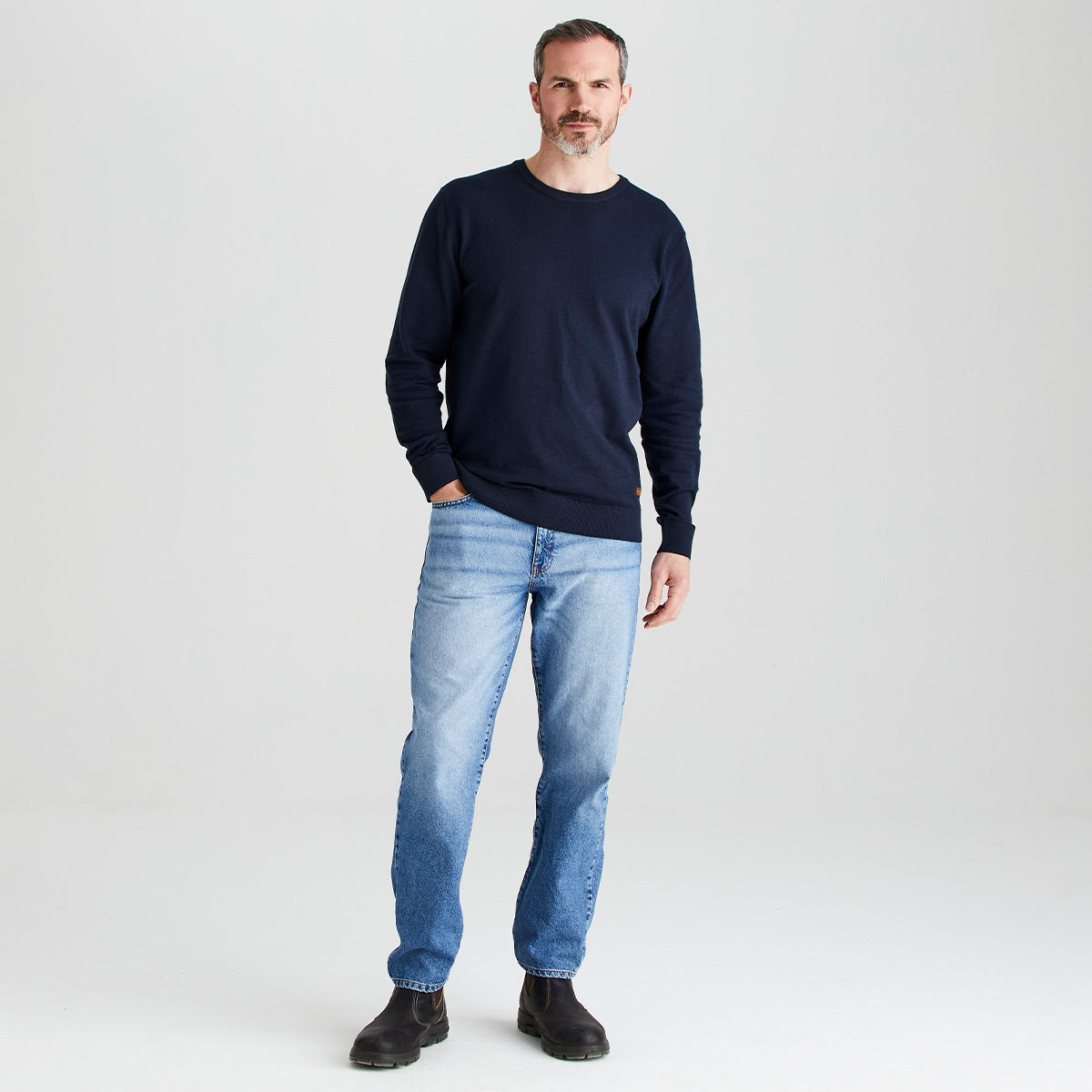 Man wearing a navy sweater and light blue jeans on a white background
