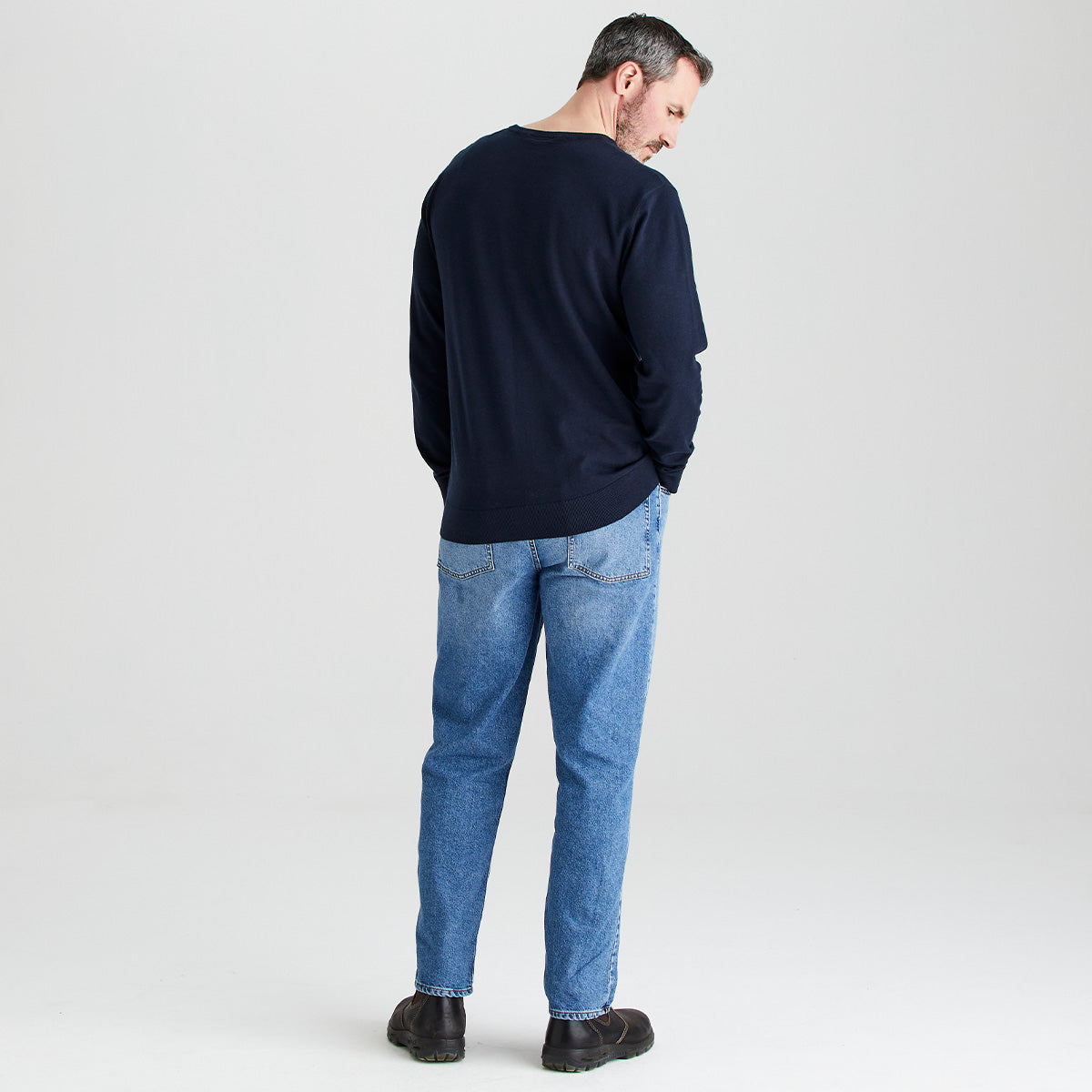 Man wearing a navy sweater and blue jeans on a light gray background