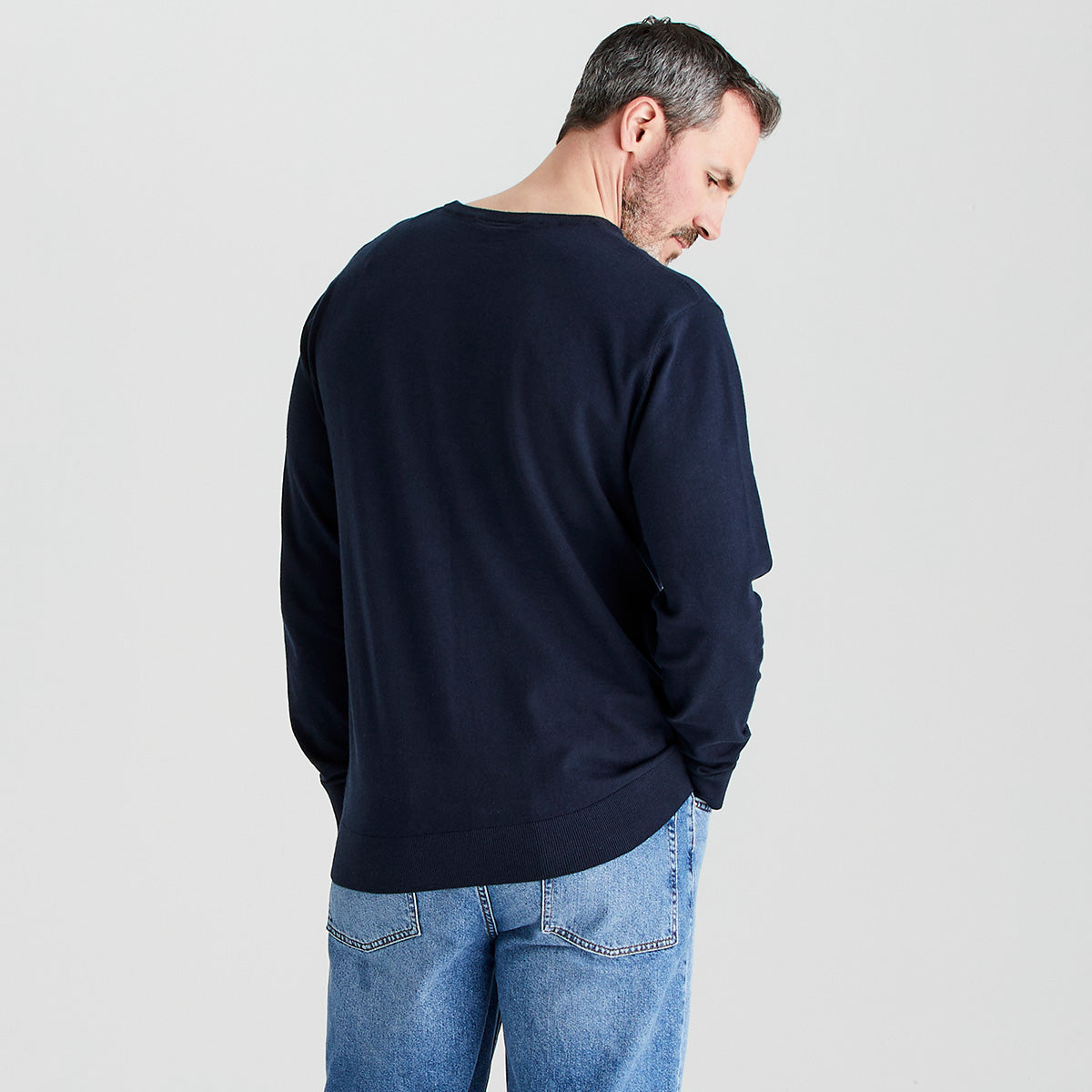Man wearing a navy sweater and blue jeans on a light gray background