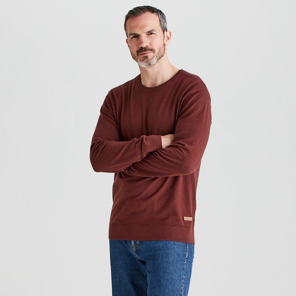 Man wearing a brown sweater and blue jeans on a light gray background