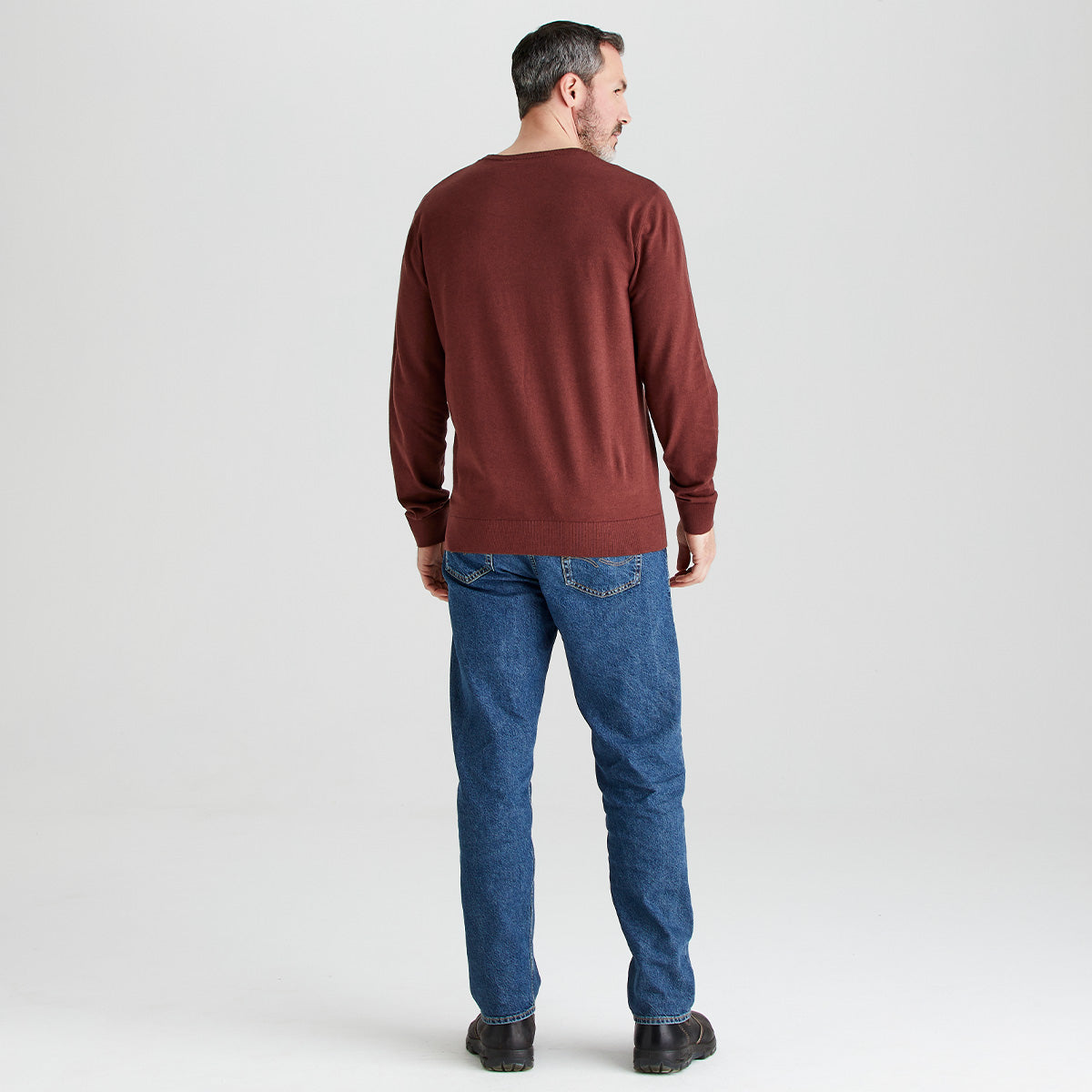 Man wearing a brown sweater and blue jeans on a white background