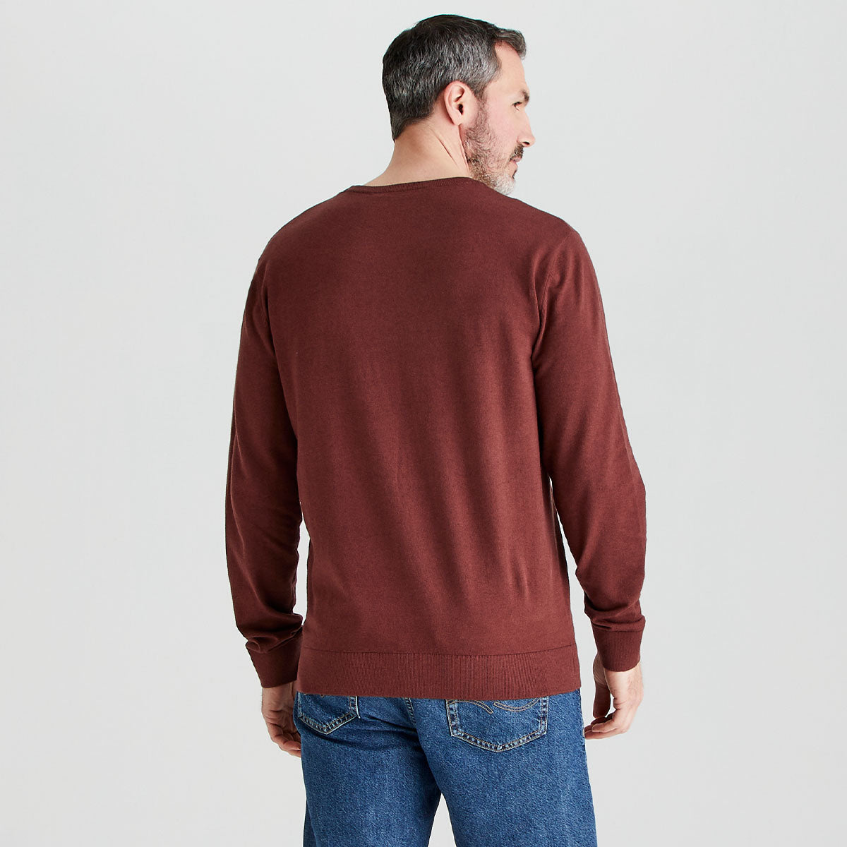 Man wearing a brown sweater and blue jeans on a light gray background