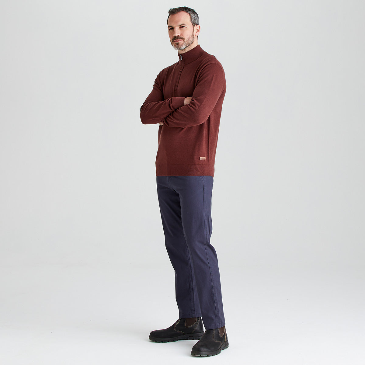 Man wearing a brown sweater and navy pants on a white background