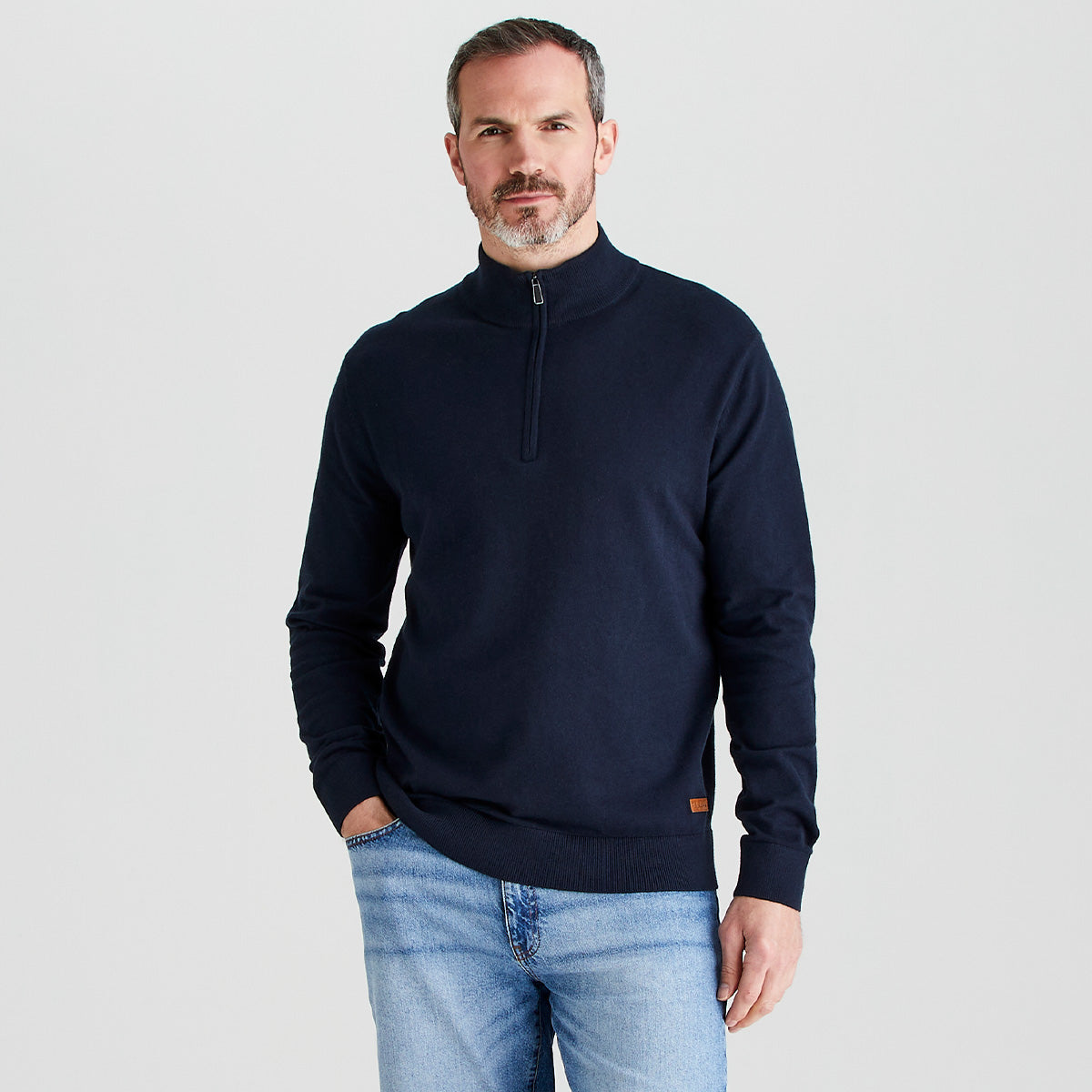 Man wearing a navy half-zip sweater and light blue jeans on a white background