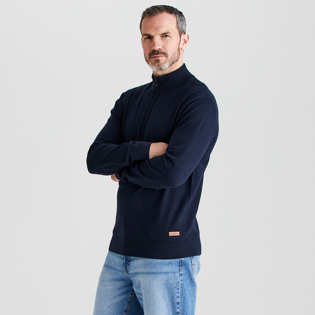 Man wearing a navy blue sweater with a small logo on a light gray background