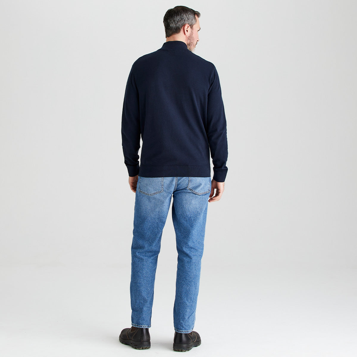 Man wearing a navy sweater and blue jeans on a light gray background