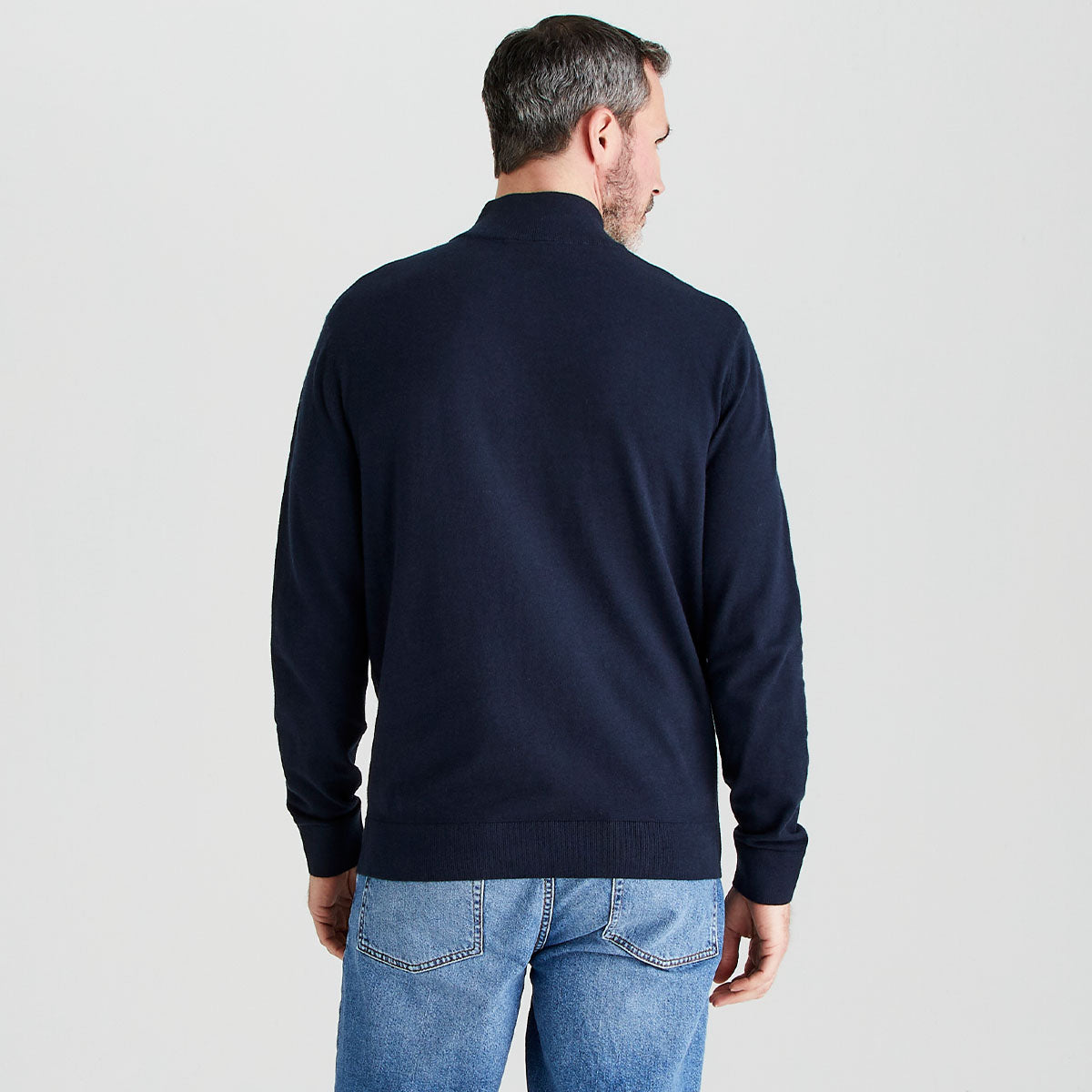 Man wearing a navy sweater and blue jeans on a light gray background