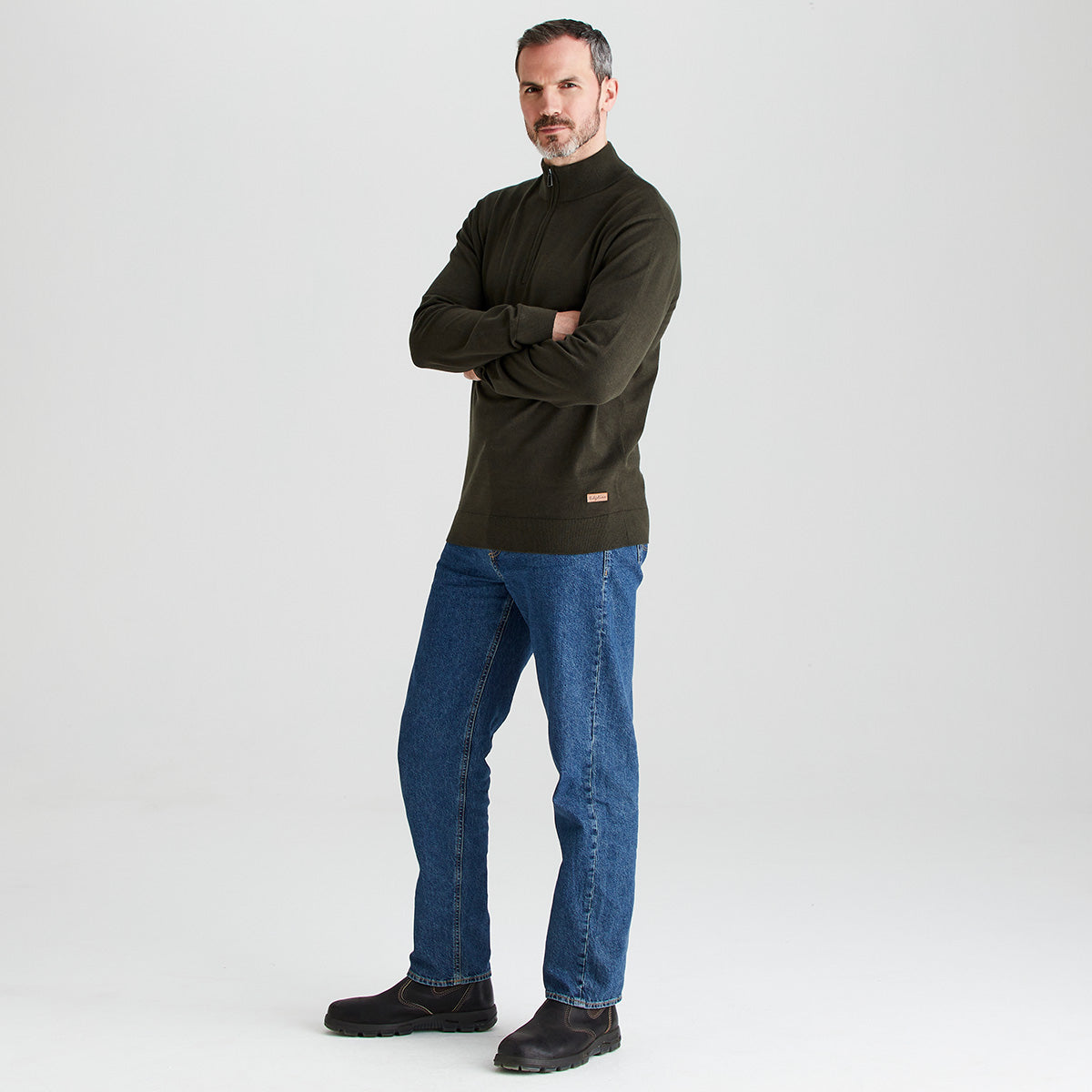 Man wearing a dark green sweater and blue jeans standing against a white background
