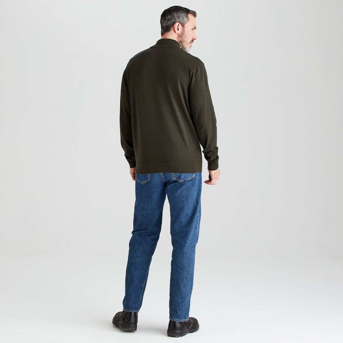 Man wearing a green sweater and blue jeans on a white background
