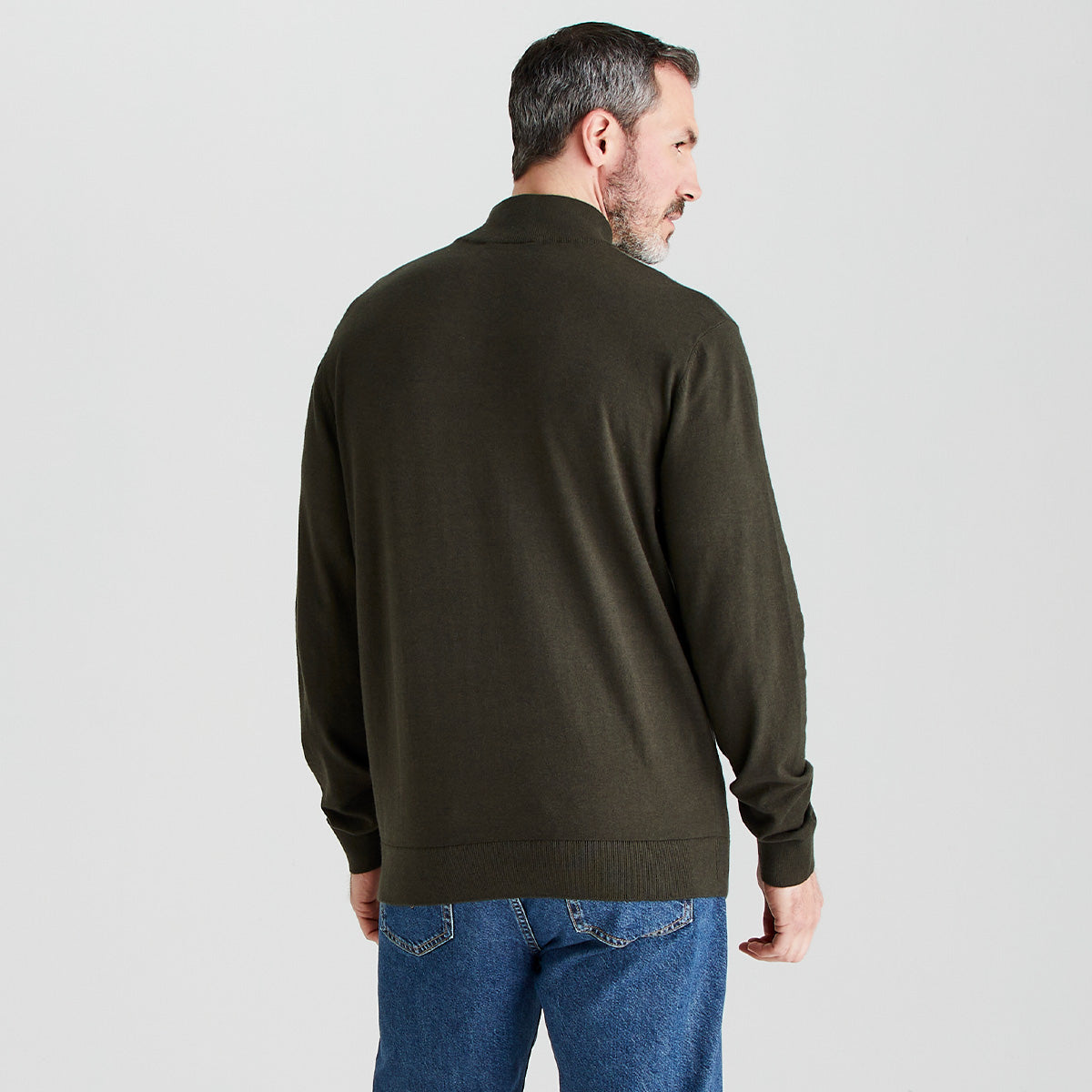 Man wearing a dark green sweater and blue jeans on a light gray background