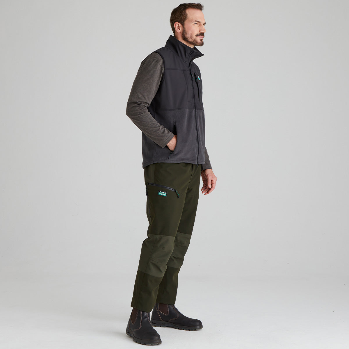 Man wearing a black vest and green pants on a grey background