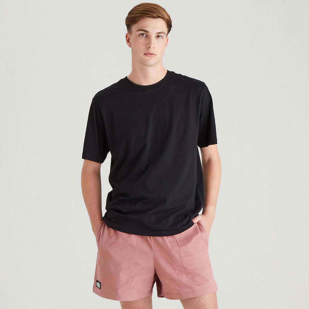 Person wearing a black t-shirt and pink shorts on a light gray background