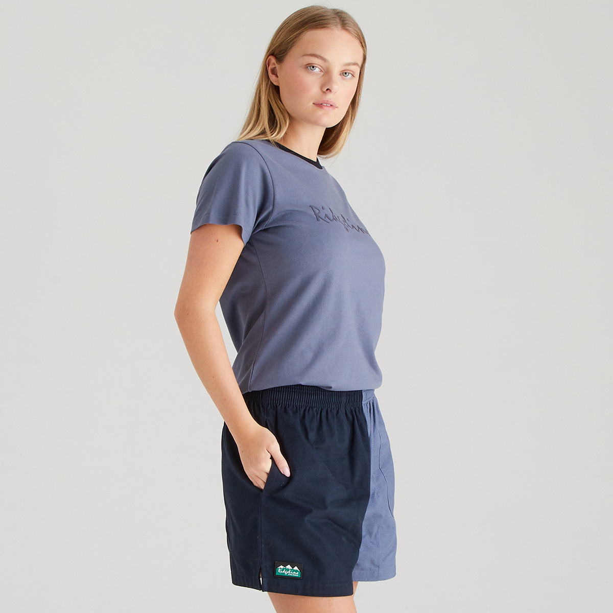 Woman wearing a blue t-shirt and navy shorts on a gray background