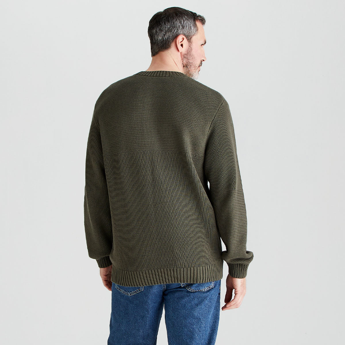 Man wearing a green sweater and blue jeans on a light gray background