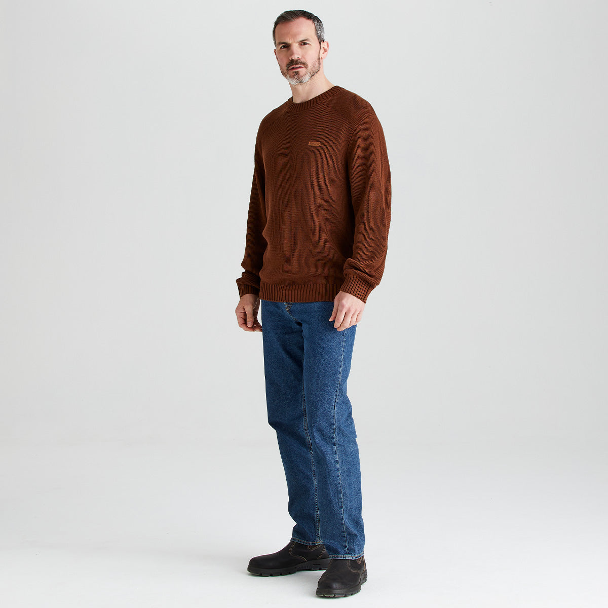 Man wearing a brown sweater and blue jeans on a white background