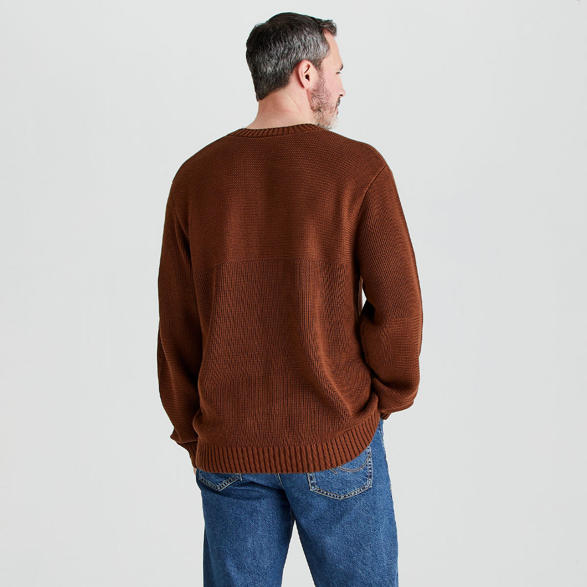 Man wearing a brown sweater and blue jeans on a light gray background