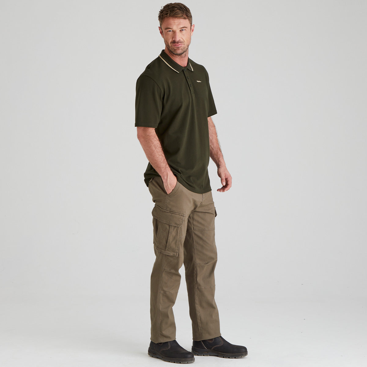 Man wearing a green polo shirt and brown cargo pants on a light gray background