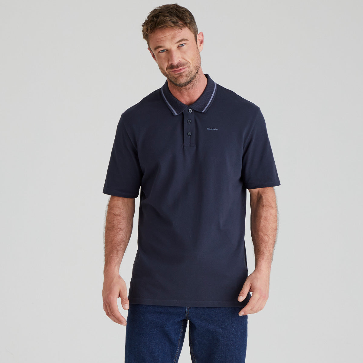 Man wearing a navy polo shirt with a Ridgeline Signature brand logo on a light grey background