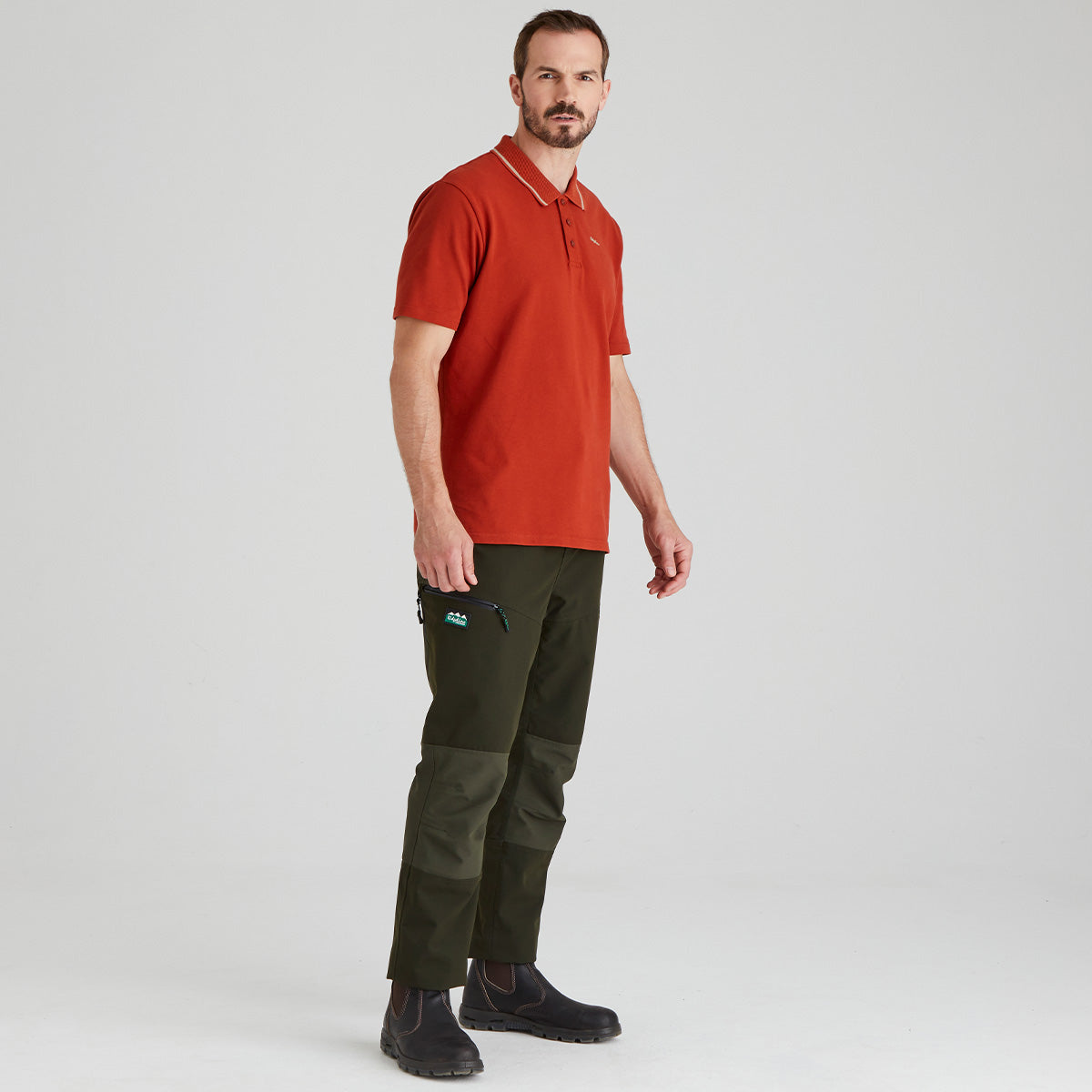 Man wearing a orange polo shirt and green pants on a light grey background